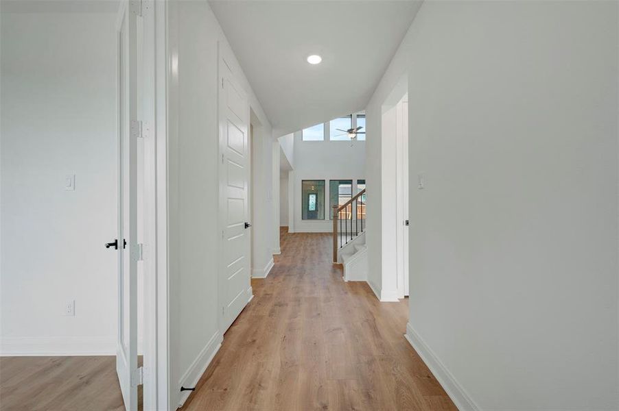 Hallway featuring light wood finished floors, vaulted ceiling, and recessed lighting