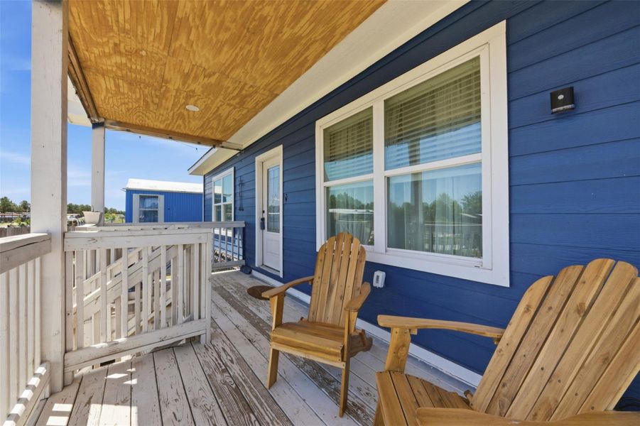 Charming front porch with wooden deck and railing, featuring blue siding and two cozy wooden chairs, perfect for relaxing and enjoying the view.