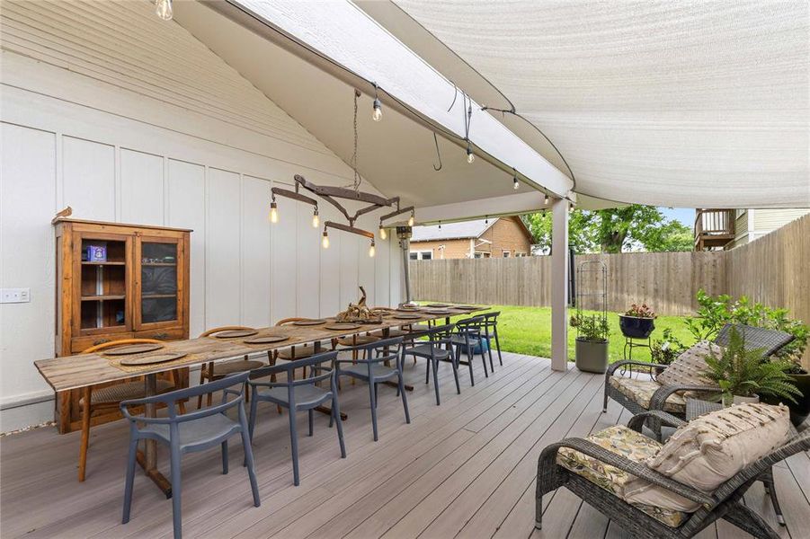 Spacious outdoor deck featuring light-colored composite flooring, a white panel accent wall, and a large shade canopy