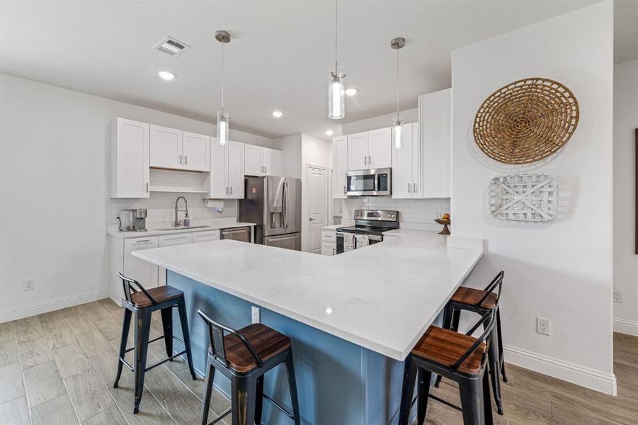 Kitchen featuring a kitchen bar, decorative backsplash, a peninsula, hanging light fixtures, and light wood-style floors