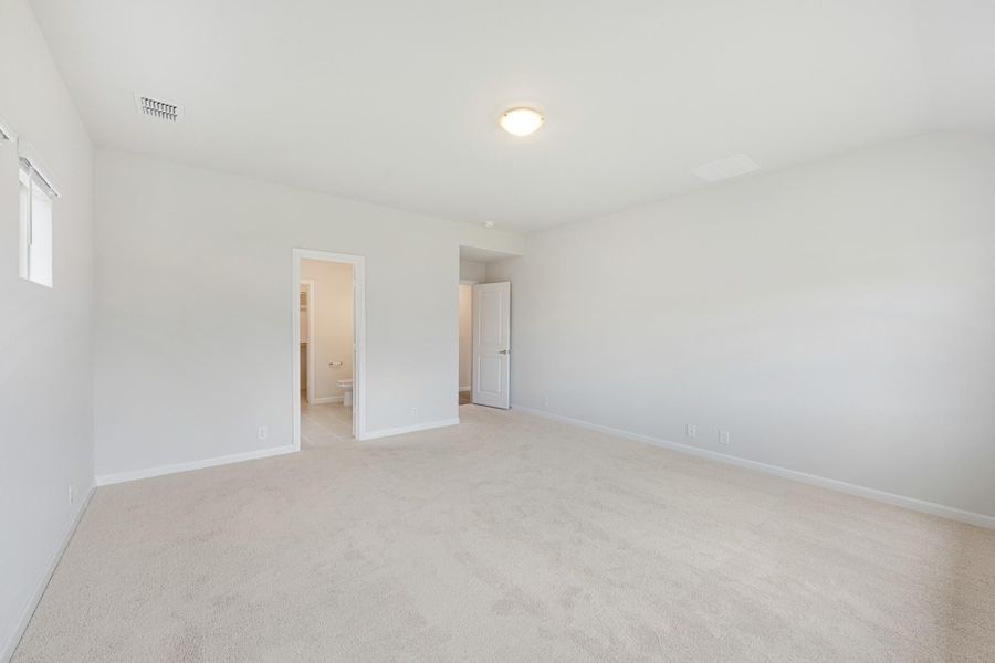 Empty bedroom with beige carpet, white walls, and doorway leading to an ensuite bathroom