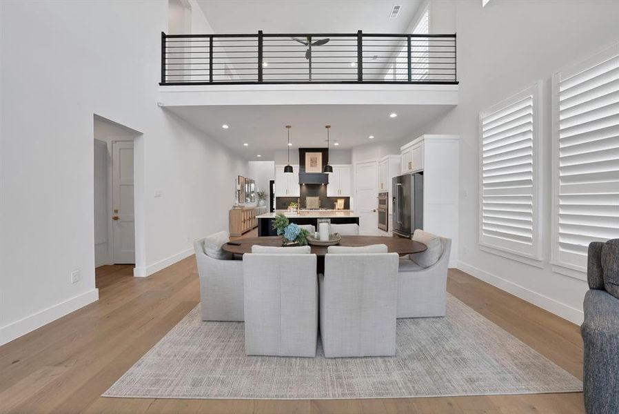 Open-concept living space featuring high ceilings, wood-finish flooring, and a second-story balcony with metal railings Open-concept living space featuring high ceilings, wood-finish flooring, and a second-story balcony with metal railings