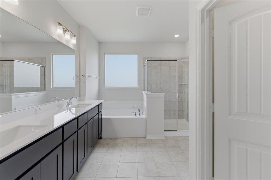 Contemporary bathroom featuring a long double vanity with dark cabinetry and light countertops, a built-in soaking tub, a separate glass-enclosed shower with tiled walls, and light tile flooring Contemporary bathroom featuring a long double vanity with dark cabinetry and light countertops, a built-in soaking tub, a separate glass-enclosed shower with tiled walls, and light tile flooring