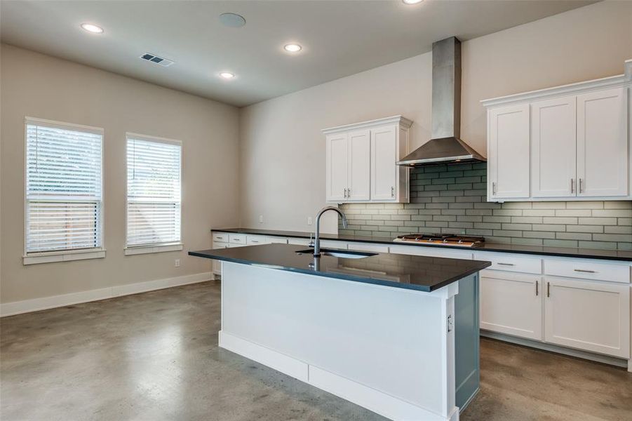 Kitchen with sink, stainless steel gas cooktop, wall chimney exhaust hood, white cabinets, and a center island with sink