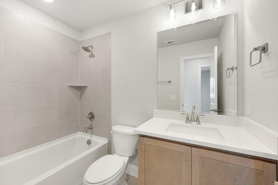 Bathroom with tub-shower combo, gray tile surround, wood vanity, and white quartz countertop