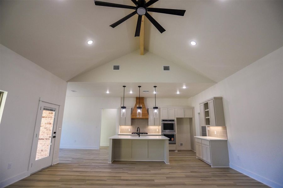 Kitchen featuring decorative backsplash, a center island with sink, light countertops, open floor plan, and beam ceiling