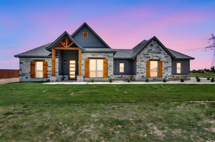 View of front of house with stone siding, a yard, and a shingled roof
