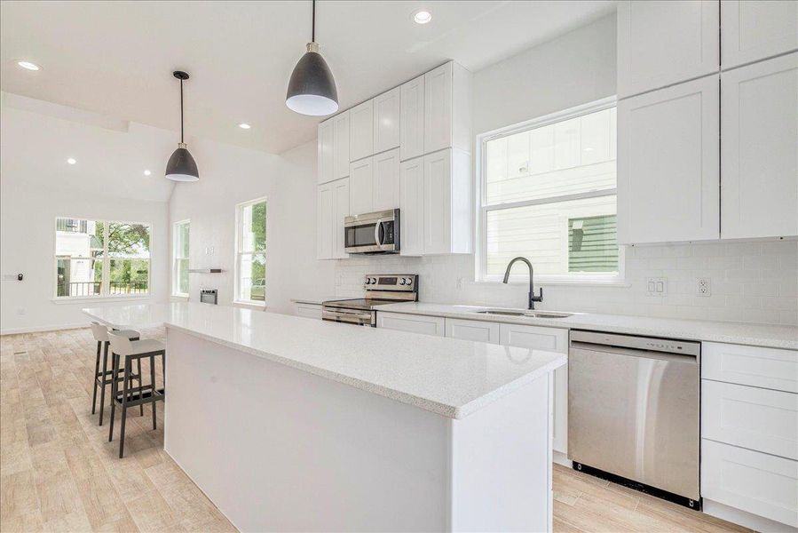 Open kitchen with eat in quartz countertop and stainless steel appliances.