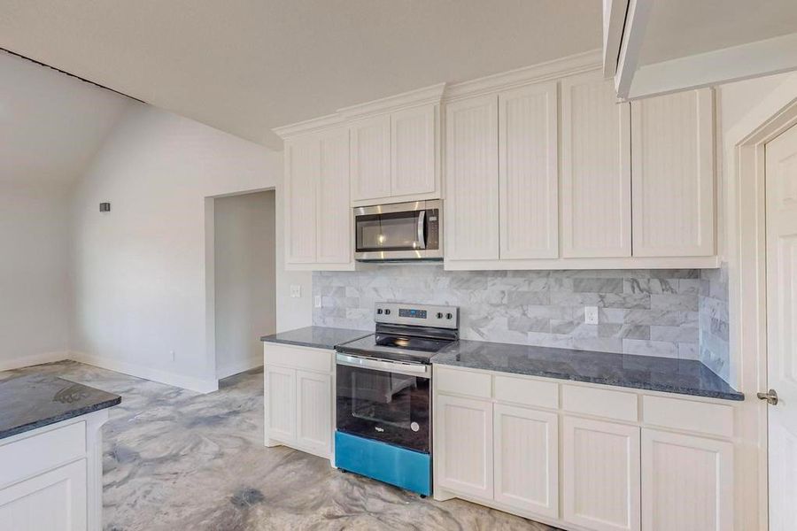 Kitchen featuring light tile patterned flooring, lofted ceiling, decorative backsplash, stainless steel appliances, and white cabinets