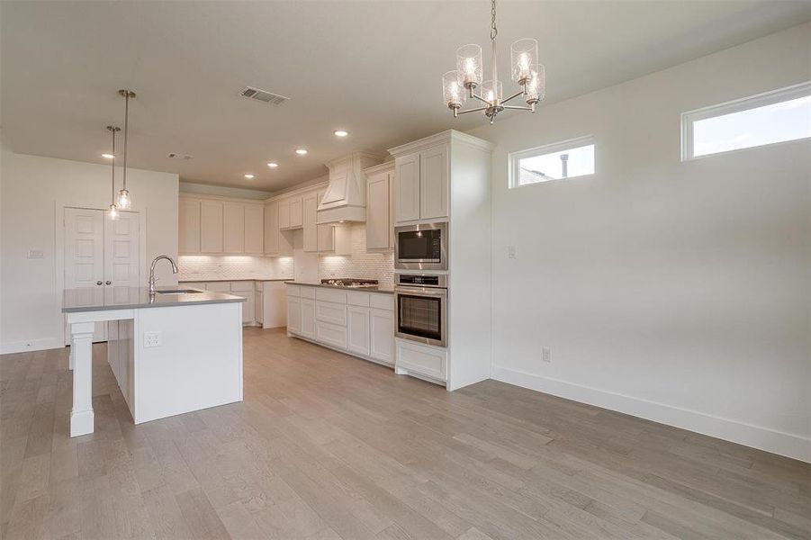 Kitchen featuring custom range hood, stainless steel appliances, white cabinets, a kitchen island with sink, and tasteful backsplash