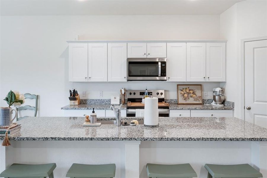 Kitchen featuring a multi-tone granite countertop island with a stainless steel sink, white shaker-style cabinetry, and stainless steel appliances