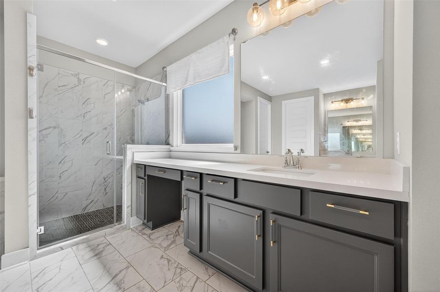 Dual vanities offer generous counter space and storage, highlighted by sleek black cabinetry and brushed gold hardware. Adjacent to the walk-in shower, the layout blends elegance with practicality