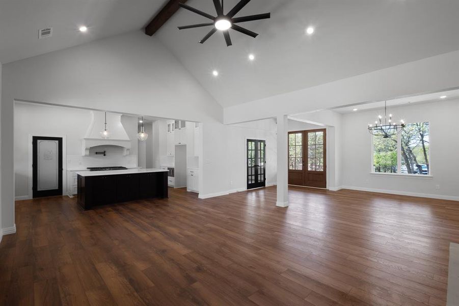 Unfurnished living room with recessed lighting, beam ceiling, dark wood finished floors, high vaulted ceiling, and ceiling fan with notable chandelier