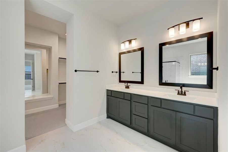 Full bath featuring healthy amount of natural light, double vanity, light marble finish flooring, and a stall shower