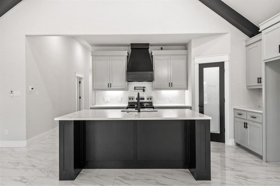 Kitchen featuring stainless steel electric range oven, light stone countertops, light marble finish floors, decorative backsplash, and a center island with sink
