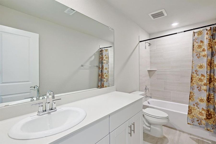 Full bathroom with shower / bathtub combination with curtain, tile floors, toilet, and vanity with extensive cabinet space