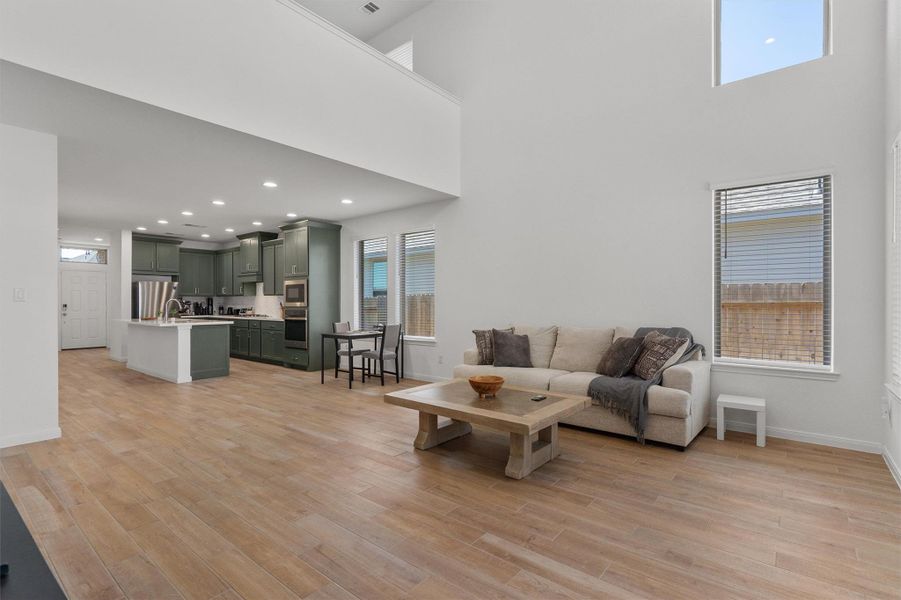 Living room with light wood-type flooring, a high ceiling, and recessed lighting
