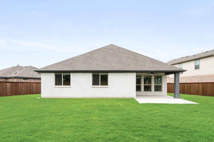 Rear view of single-story brick home with covered patio, large green lawn, and wood privacy fence Rear view of single-story brick home with covered patio, large green lawn, and wood privacy fence