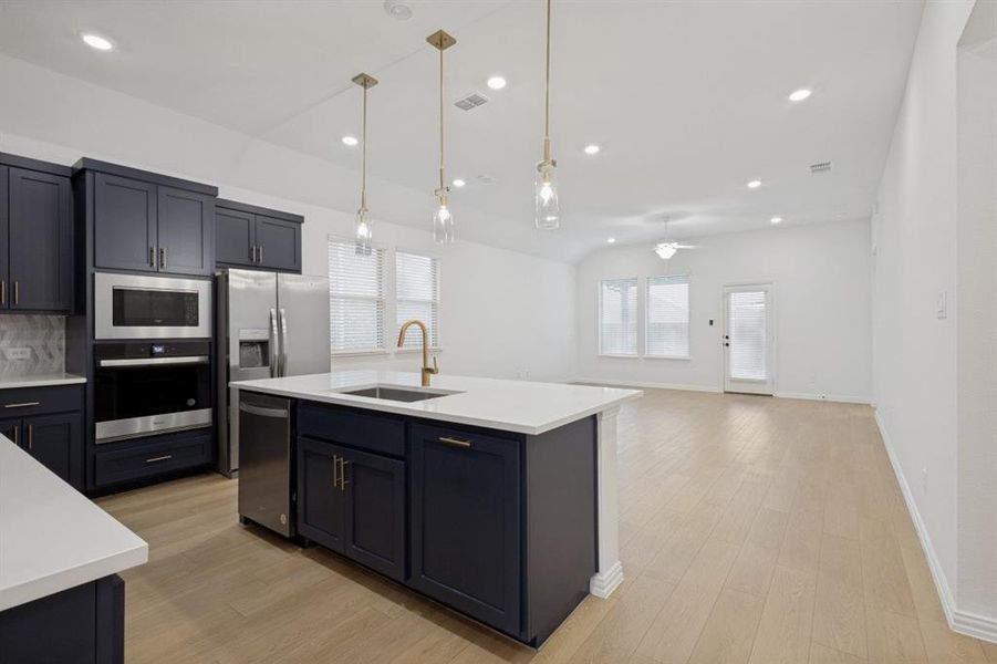 Open-concept kitchen featuring dark cabinetry, stainless steel appliances, and a central island with a sink and pendant lighting
