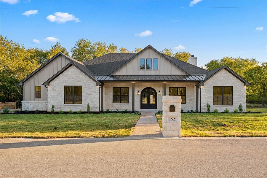 Modern farmhouse style home with stone siding, covered porch, board and batten siding, and a front yard