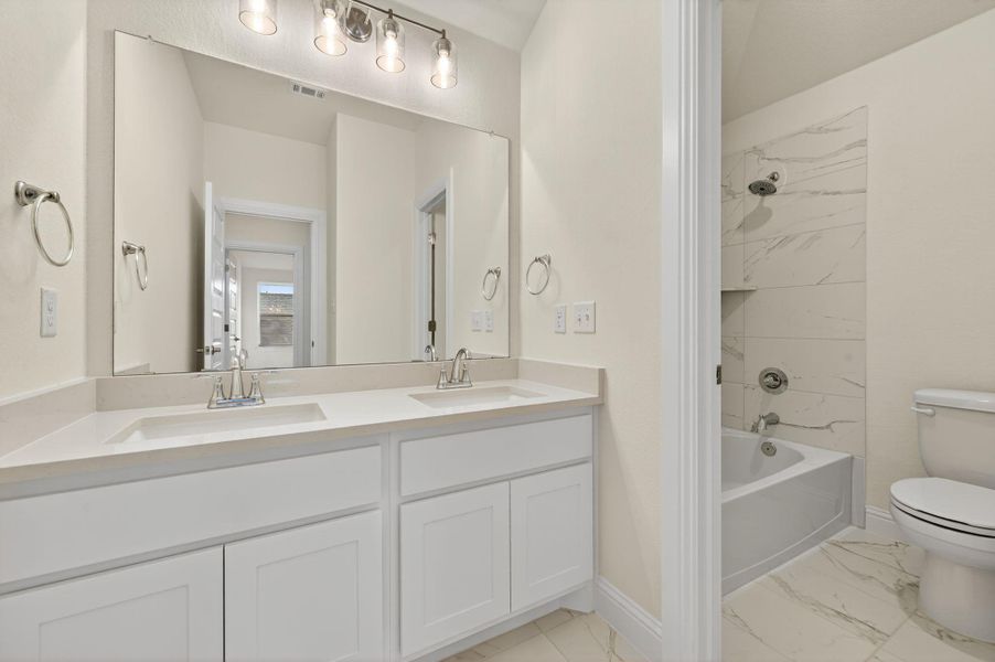 Bathroom featuring washtub / shower combination, double vanity, and light marble finish flooring
