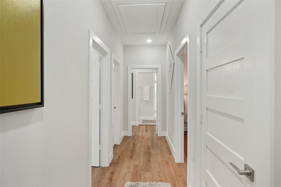 2nd floor hallway leading to the primary suite at the end of the hallway and the two secondary bedrooms and secondary bathroom on wither side of the hallway. Immediately to the right is the laundry closet with electric dryer connections and black hexagonal tile flooring.