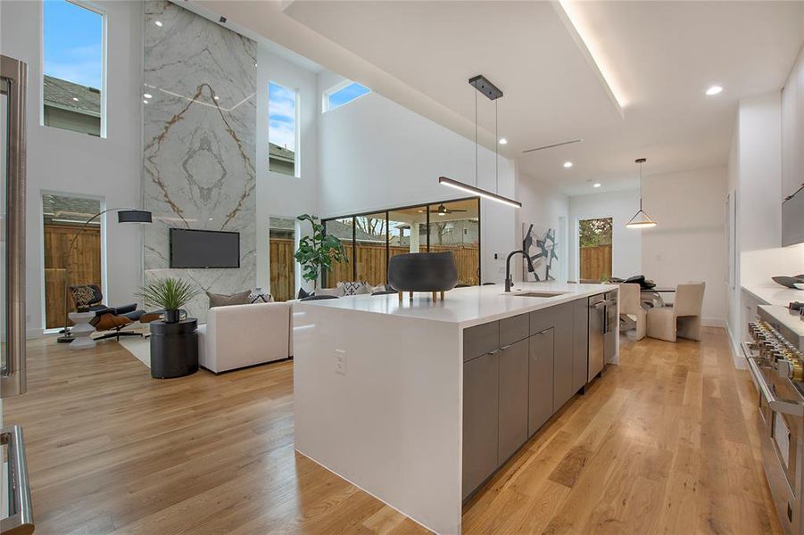 Kitchen with high end stainless steel range oven, sink, gray cabinets, hanging light fixtures, and a large island