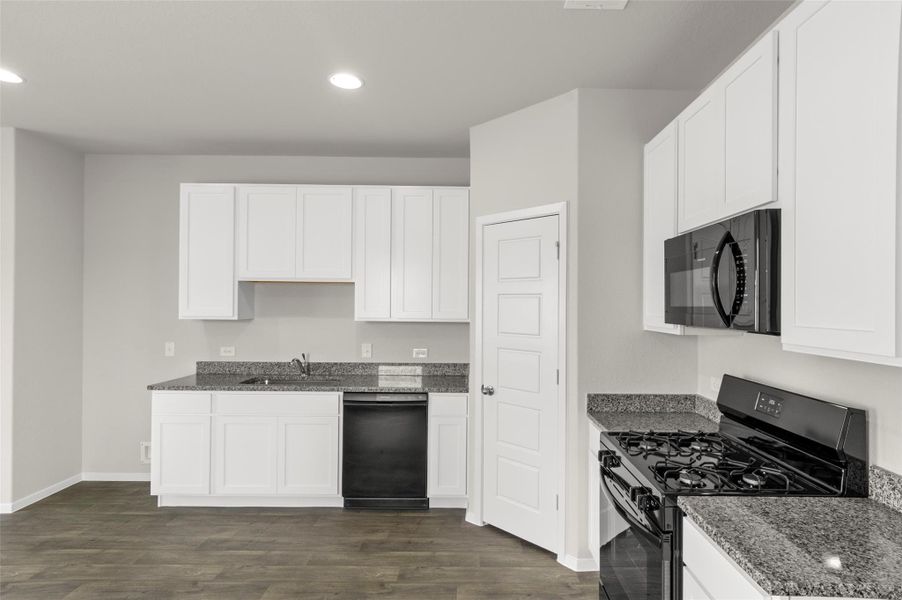 Kitchen with black appliances, dark stone countertops, recessed lighting, dark wood-type flooring, and white cabinetry Kitchen with black appliances, dark stone countertops, recessed lighting, dark wood-type flooring, and white cabinetry