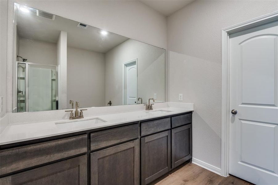 Bathroom with double vanity, light wood-style floors, and a shower stall