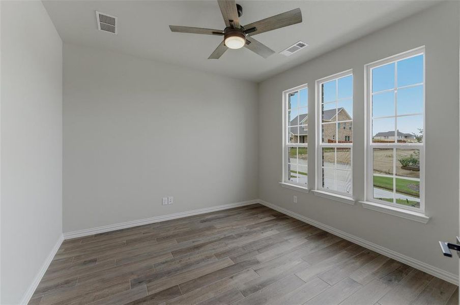 Room featuring three tall windows with white trim, wood-finish flooring, a ceiling fan with integrated lighting, and neutral wall paint