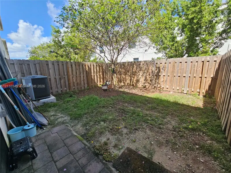 Fenced backyard featuring a paver patio, established tree, and grass area