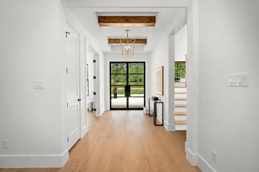 Inviting foyer featuring wide-plank luxury vinyl flooring, exposed beam accents, designer lighting, and modern steel-framed front doors. Inviting foyer featuring wide-plank luxury vinyl flooring, exposed beam accents, designer lighting, and modern steel-framed front doors.