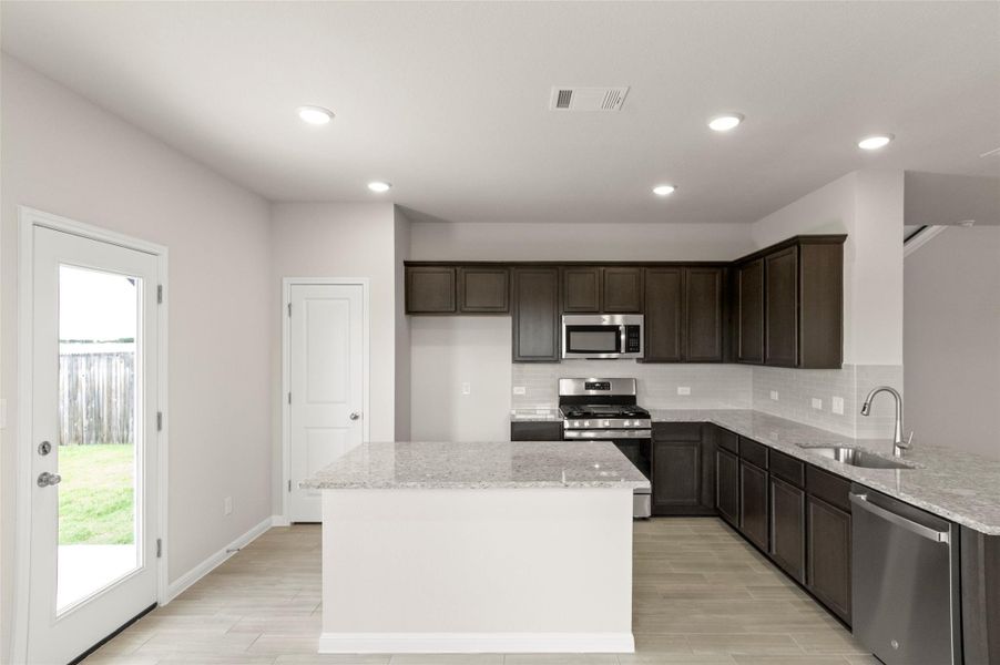 Kitchen featuring appliances with stainless steel finishes, tasteful backsplash, light stone countertops, light wood-style flooring, and recessed lighting