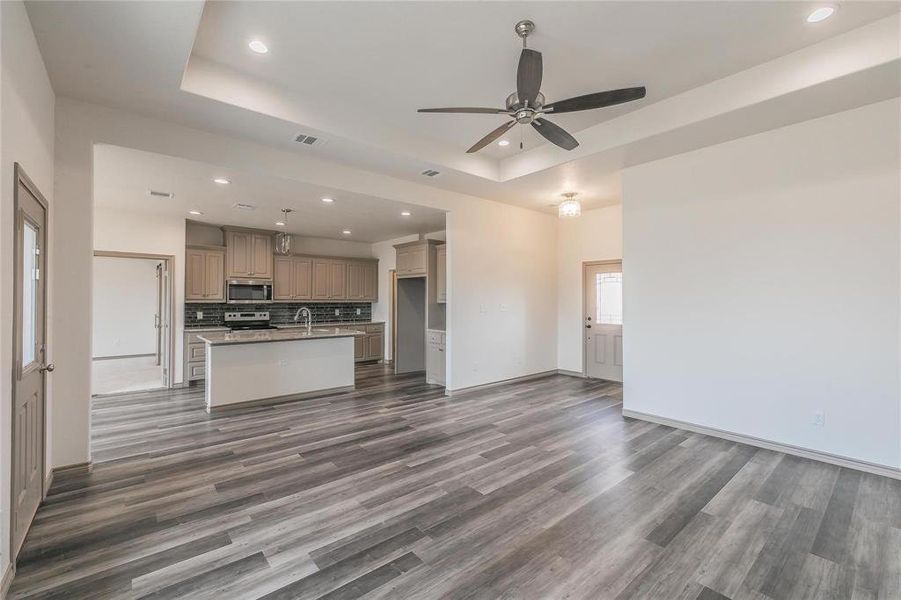 Unfurnished living room featuring a raised ceiling, recessed lighting, dark wood-type flooring, and a ceiling fan