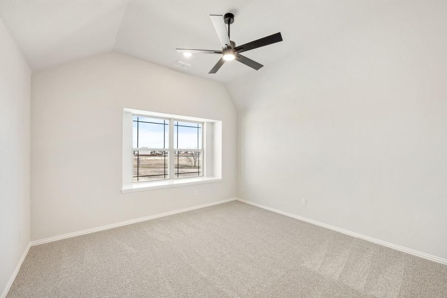 Empty bedroom with vaulted ceiling, ceiling fan, carpet flooring, and large window with outdoor view