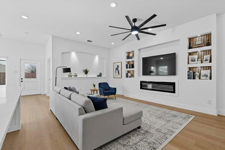 Living area with built in shelves, ceiling fan, light wood finished floors, a glass covered fireplace, and recessed lighting