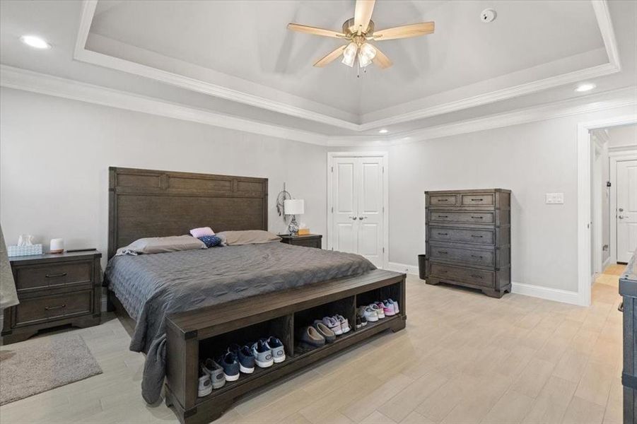 Bedroom featuring light wood finished floors, baseboards, a raised ceiling, and ornamental molding