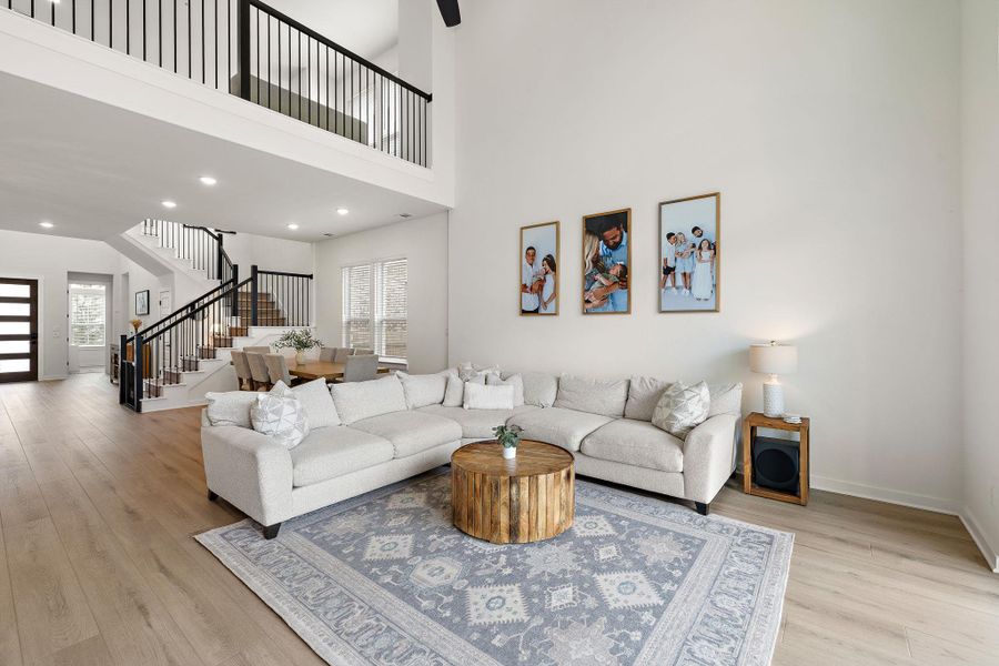 Two-story living area featuring light wood-finish flooring, recessed lighting, and a prominent staircase with black wrought iron balusters