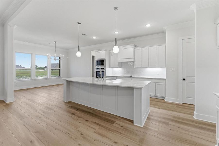 Central kitchen island with a stone-finish countertop, pendant lighting, and light wood-finish flooring throughout Central kitchen island with a stone-finish countertop, pendant lighting, and light wood-finish flooring throughout