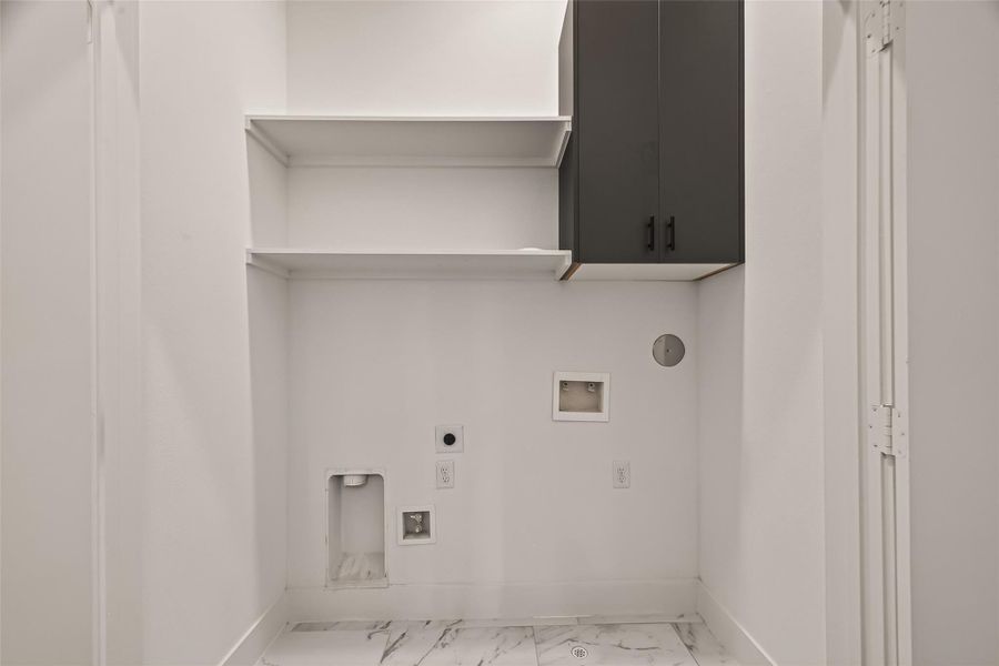 This is a laundry room with white walls and a marble-patterned tile floor. It features built-in shelves, dark cabinetry for storage, and hookups for a washer and dryer. This is a laundry room with white walls and a marble-patterned tile floor. It features built-in shelves, dark cabinetry for storage, and hookups for a washer and dryer.