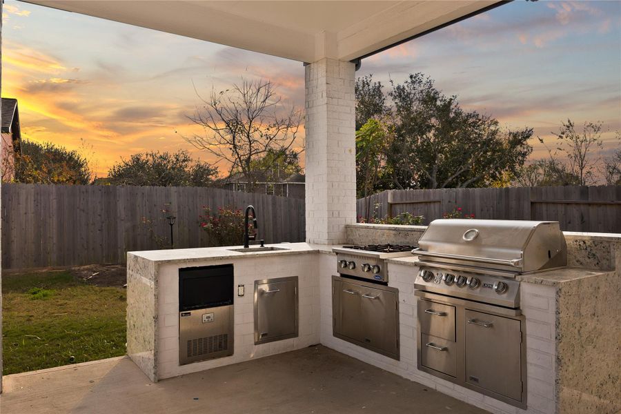 This photo showcases a stylish outdoor kitchen with a built-in grill and stove, set against a vibrant sunset backdrop. The space is enclosed by a wooden fence, offering privacy and a cozy atmosphere for entertaining or relaxing outdoors. This photo showcases a stylish outdoor kitchen with a built-in grill and stove, set against a vibrant sunset backdrop. The space is enclosed by a wooden fence, offering privacy and a cozy atmosphere for entertaining or relaxing outdoors.