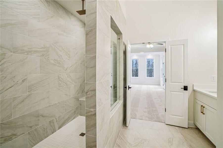 Primary bathroom walk in shower features rainhead shower head, wand and bench- light and bright finishes- image is of previous finished unit.