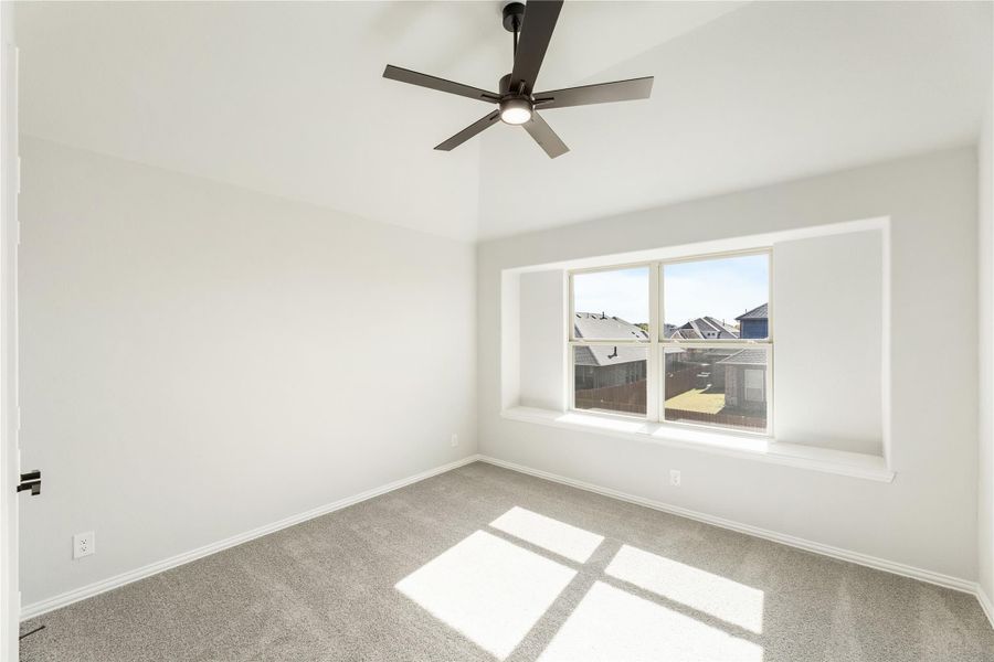 Empty bedroom with gray carpet, ceiling fan, and large window with neighborhood view