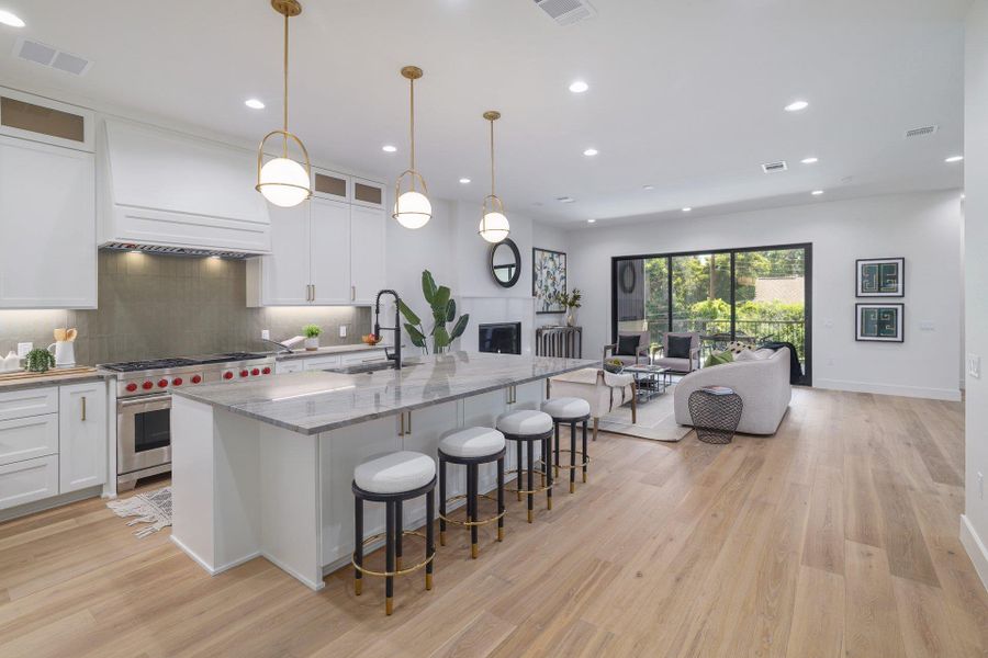 Open-concept living area featuring a kitchen island with seating, pendant lighting, stainless steel range with custom hood, wood-finish flooring, and a fireplace