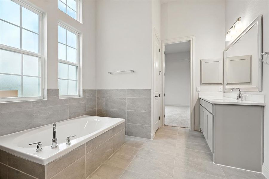 Bathroom with healthy amount of natural light, vanity, light tile patterned flooring, a garden tub, and tile walls