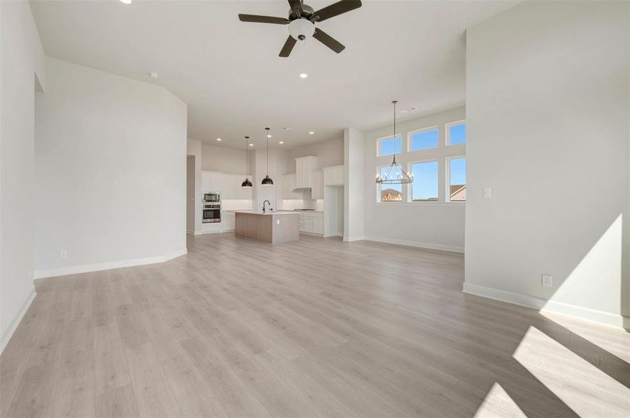 Spacious open-concept interior featuring light wood-finish flooring, high ceilings, a modern ceiling fan, and extensive natural light from multiple windows