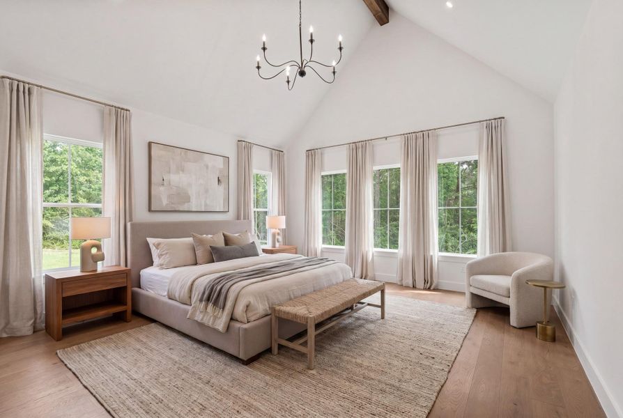 Spacious primary suite with vaulted ceilings and exposed reclaimed barnwood beam creating an open, airy feel. Walls of windows flood the room with natural light and frame peaceful backyard views. 7" white oak plank wood flooring continues throughout, adding warmth and continuity. Generous square footage provides ample space for a true retreat setup, all positioned on the main level for privacy and comfort.