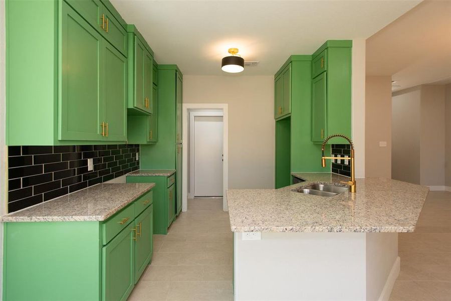 Kitchen featuring sink, light stone counters, green cabinets, and tasteful backsplash