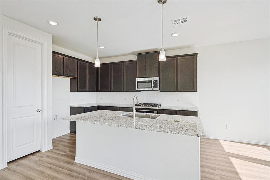 Kitchen with light hardwood / wood-style flooring, a kitchen island with sink, sink, and hanging light fixtures