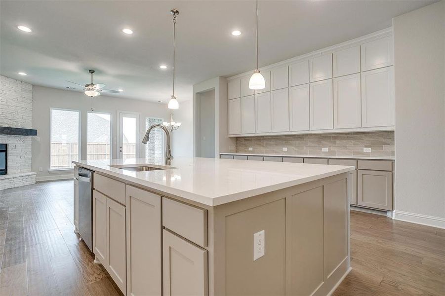 Kitchen with ceiling fan with notable chandelier, a fireplace, light wood-type flooring, a center island with sink, and sink